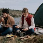 Campgrounds - A Man and a Woman Eating while Sitting on the Ground