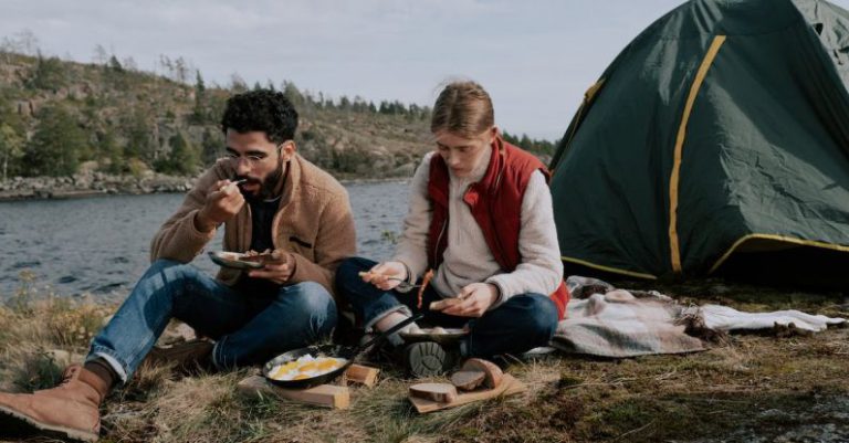 Campgrounds - A Man and a Woman Eating while Sitting on the Ground